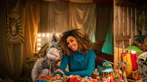 Een foto van Ezel Chiel die binnen naast een vrouw aan een tafel zit.  Er staan veel verschillende spullen op tafel. 