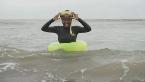 Een foto van presentator Tirsa in zeewater in een zwemband. Ze heeft een snorkel en duikbril op. Ze heeft de duikbril op haar voorhoofd en houdt die met beide handen vast.