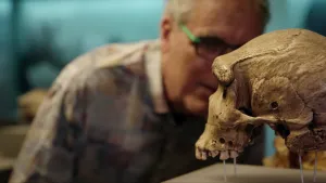 Een foto van wetenschapsjournalist Govert. Hij kijkt aandachtig naar een hele oude schedel van een mens. De schedel zie je op de voorgrond. De kaak van de schedel ontbreekt.