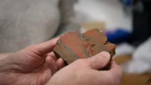 Een foto van twee handen die een stuk steen vasthouden. Er zitten verschillende lagen in de steen waaronder een ijzer lagen.