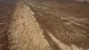 Een foto van een droog gebied in Californië in Amerika waar door het midden een breuklijn loopt. Langs de breuklijn zijn heuvels van zand te zien. Een breuklijn is een kronkelende lijn die de aardkorst in meerdere stukken verdeeld.  