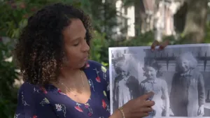 Een foto van de presentator. Ze toont een zwartwit-foto uit de Tweede Wereldoorlog. Daarop zijn drie jonge meisjes te zien. Ze dragen allemaal een Jodenster op hun kleding. De presentator wijst naar een van die Jodensterren.