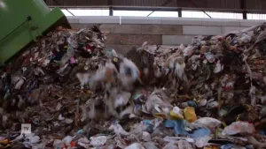 Een foto van een hele berg plastic afval. Het is ergens binnen. Op de foto zie je dat er nog meer plastic afval bij gestort wordt.
