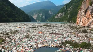Een foto van een meer tussen bergen. In het meer ligt heel veel plastic afval. 