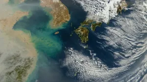 Een foto genomen vanuit de ruimte. Je ziet een stukje van de aarde, met land en zee en wolken.