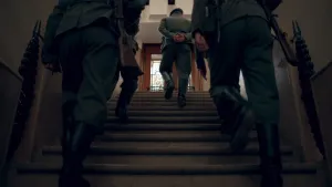 Een foto van een vier mannen in legeruniformen die een stenen trap op lopen. Je ziet hen van achter. De ruimte is donker. De mannen dragen geweren en hebben laarzen aan. 