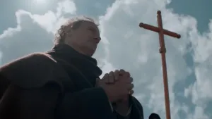 Een foto van een gelovige die aan het bidden is. Op de achtergrond is er een houten kruis zichtbaar.