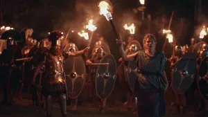 Een foto van een groep Romeinse soldaten die in het donker met wapens, schilden en fakkels staan. Voor hen staat er een generaal en een vrouw met beide een fakkel in hun handen.