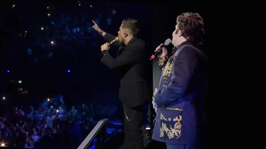 Een foto van de zanger André Hazes en een andere zanger. Ze staan te zingen voor een groot publiek.