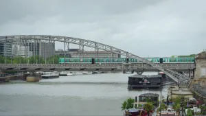 Een foto van een stad met een brug over een rivier. Over die brug rijdt een groenkleurige metro. In de rivier liggen woonboten. 