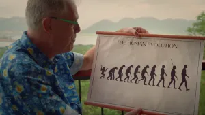 Een foto van wetenschapsjournalist Govert. Hij houdt een tekening vast. Daarom zie je de evolutie van de mens afgebeeld. Het begint met een aapachtige. Daarnaast zie je een steeds meer rechtop lopende mens. 