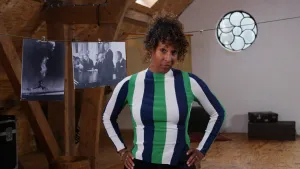 Een foto waar een presentator recht voor de camera staat. Op de achtergrond hangt er een lijn met een zwartwit foto van een ontploffing van een kernbom en een zwartwit foto waar mensen een afspraak tekenen.