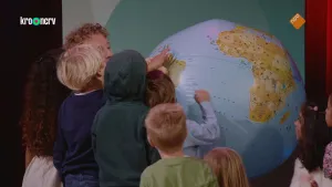 Een foto van een vijf jonge kinderen en een man. Sommige houden hun hand op een grote opblaasbal in de vorm van de Aarde. Ze kijken daarbij naar Zuid-Amerika.