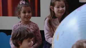 Een foto van drie kleine kinderen. Ze kijken naar een opblaasbal in de vorm van de Aarde. Ze zijn blij.