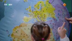 Een foto van een grote opblaasbal in de vorm van de Aarde. Alle landen zijn erop aangegeven. Iemands vinger wijst naar een land in Azië. Op de voorgrond zie het hoofd van een meisje. Zij steekt een wijsvinger omhoog.