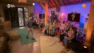 Foto van een studioachtige ruimte waarin veel kinderen op een rij zitten, een man loopt naar ze toe.