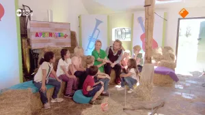 Foto van studioachtige ruimte waarin kinderen en een man en vrouw bij elkaar zitten, er liggen balen hooi op de grond.