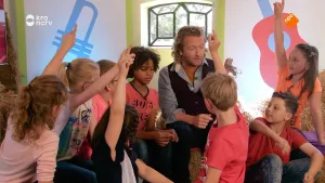 Foto van ruimte waarin kinderen rondom een man zitten.