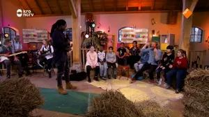 Foto van studioachtige ruimte waarin vrouw iets staat te vertellen aan kinderen en een man die er zitten, op de grond ligt hooi.