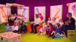 Foto van vele kinderen en een man die in een vrolijke kamer zitten, er staat een ouderwetse ijscokar.