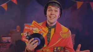 Een foto van een presentator in rood met lichtbruine carnavalskleding, een bruine hoed op en kleurige speltjes op zijn borst. In zijn handen heeft hij platen met carnavalsmuziek. Twee artiesten "Wim Kersten en De Viltjes" en "Arie Ribbens"zijn leesbaar.