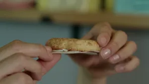 Een foto van twee handen die een koekje met de naam kokosmakroon vasthouden. De bodem van de kokosmakroon is van snoeppapier.