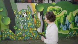 Een foto van presentator Wieteke die naar een illustratie staat te kijken van een boos monster met een open mond vol met scherpe tanden.