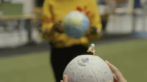 Een foto van twee handen die een opblaasversie van de maan vasthouden. Op de maan staat een LEGO poppetje met een astronautenpak aan. Op de onscherpe achtergrond staat iemand met een opblaasversie van de planeet aarde in zijn of haar handen.