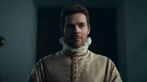 Een foto van een man verkleed als Willem van Oranje. De man heeft een witte kraag om zijn nek. Hij heeft een lichtbruin pak aan met donkerbruine randen bij de nek, bovenarmen en naast de knopen van zijn kostuum. Hij kijkt naar een punt achter de camera.