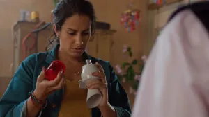 Een foto van Zonia die kijkt naar een alarm dat ze vastheeft. In haar linkerhand heeft ze het witte, plastic deel met het lampje erop vast. In haar rechterhand heeft ze het rode plastic kapje van het alarm. Voor Zonia is de arm van iemand anders te zien.