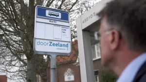 Een foto van een gezicht van een man en een hoek van een bushokje in de provincie Zeeland. De man kijkt naar een bord waar normaal de buslijnen staan. De haltenaam "Markt" en de vervoerder staan erop en "Haltetaxi", een taxi die mensen zelf moeten bellen.