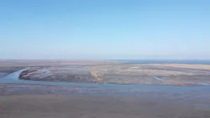 Een foto van de Hedwigepolder vanuit de blauwe lucht genomen. Het poldergebied is heel nat en naast stroken water is ook de grond eromheen heel nat van het water. De grond is verder kaal zonder bomen of planten. 