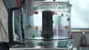 Een foto van een keukenmachine, die gekleurde chocoladebolletjes aan het hakken is.