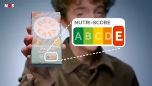 Een foto van een presentator die een chocoladereep omhoog houdt. De Nutri-score die op de voorkant van de chocoladereep zichtbaar is, is extra groot naast de chocoladereep op de foto weergegeven.