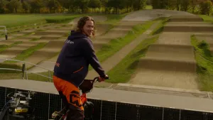 Een foto van presentator Pascal die op BMX fiets aan de start staat van een hindernis baan met veel heuveltjes. Een BMX fiets is een kleine fiets gemaakt om mee te stunten.