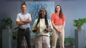 Een foto van presentator Tirsa die in het midden staat. Links en rechts van haar staat een man en een vrouw. Op de achtergrond is er een groot schilderij te zien van hersenen.