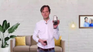 Een foto van een presentator die kijkt naar een kleine metronoom die hij omhoog houdt met zijn linkerhand. Een metronoom is een apparaat om het tempo van muziek of geluid mee te bepalen. 