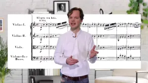 Een foto van een presentator met daarachter een gedeelte van een partituur zichtbaar. Op de partituur staan in het Italiaans van boven naar beneden de instrumenten en van links naar rechts de noten die de muzikanten van het instrument moeten spelen.