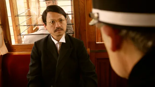 Een foto van Mahatma Gandhi die in de trein zit onderweg naar Pretoria in Zuid-Afrika. Aan de rechterkand is de achterkant van het hoofd van trein conducteur te zien.