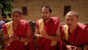 Een foto van drie Tibetaanse monniken in traditionele kleding, geel en rood en met een rode lap stof om de schouder. Iedere monnik staat op een boeddhistische manier met zijn eigen handen tegen elkaar op de foto.