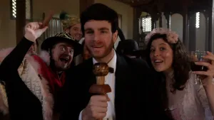 Een foto van zes feestvierende Joodse mensen die Poerim, Joods carnaval, vieren in een synagoge. De verslaggever in het midden heeft een houten microfoon vast. De mensen hebben feestelijke kleding aan en de twee vrouwen hebben een glas drinken vast.