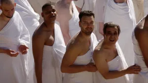 Een foto van moslims in witte gewaden die naar de camera kijken. De moslims zijn bezig zeven rondjes rond de Kaäba, het centrale heiligdom van de islam, te lopen. De Kaäba is niet zichtbaar op de foto.