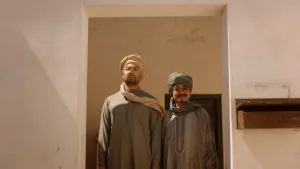 Een foto van twee Arabisch geklede moslim mannen. De mannen staan met hun rug naar een muur toe, waarin ook een deur zit.