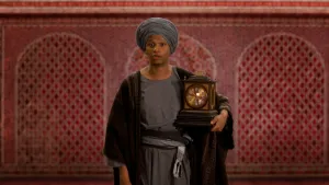 Een foto van een presentator in Arabische kleding compleet met een stoffen tulband. De presentator heeft een antieke houten klok, ook wel een pendule of slingerklok genoemd, onder zijn linkerarm.