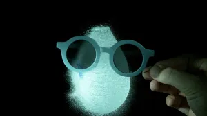 Een foto van een ballon, die net kapot wordt geprikt door een hand met een naald. Voor de ballon is een bril met donkere glazen.