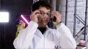 Een foto van presentator Jurre die een veiligheidsbril opzet en een gasaansteker vastheeft, om zich voor te bereiden op een experiment.