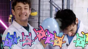 Een foto van presentatoren Jurre en Sahil. Jurre beweegt een ballon over het haar van Sahil, om het haar van Sahil statisch te maken. Op de voorgrond zijn tekeningen van konijn-achtige figuurtjes en lichtblauwe elektrische vonkjes zichtbaar.