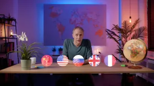Een foto van een presentator die achter een tafel zit en naar de camera kijkt. Boven de tafel zijn ronde vlaggen van China, De Verenigde Staten, Rusland, Engeland en Frankrijk. Daarnaast staat een wereldbol op de tafel.