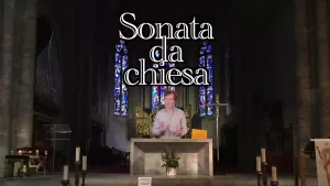 Een foto van een presentator die in een kerk achter een tafelvormige verhoging staat. Achter de presentator zijn glas-in-lood ramen zichtbaar. Boven de presentator zijn de woorden "Sonata da chiesa" te lezen.
