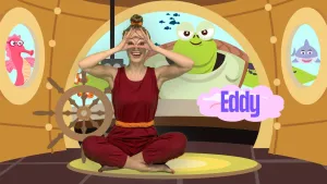 Een foto van presentator Roos die in een yogahouding op de grond zit met haar handen voor haar ogen in de vorm van een bril. Rechts staat de tekst Eddy. Ze zit in een onderzeeboot en er kijkt een grote schildpad naar binnen.